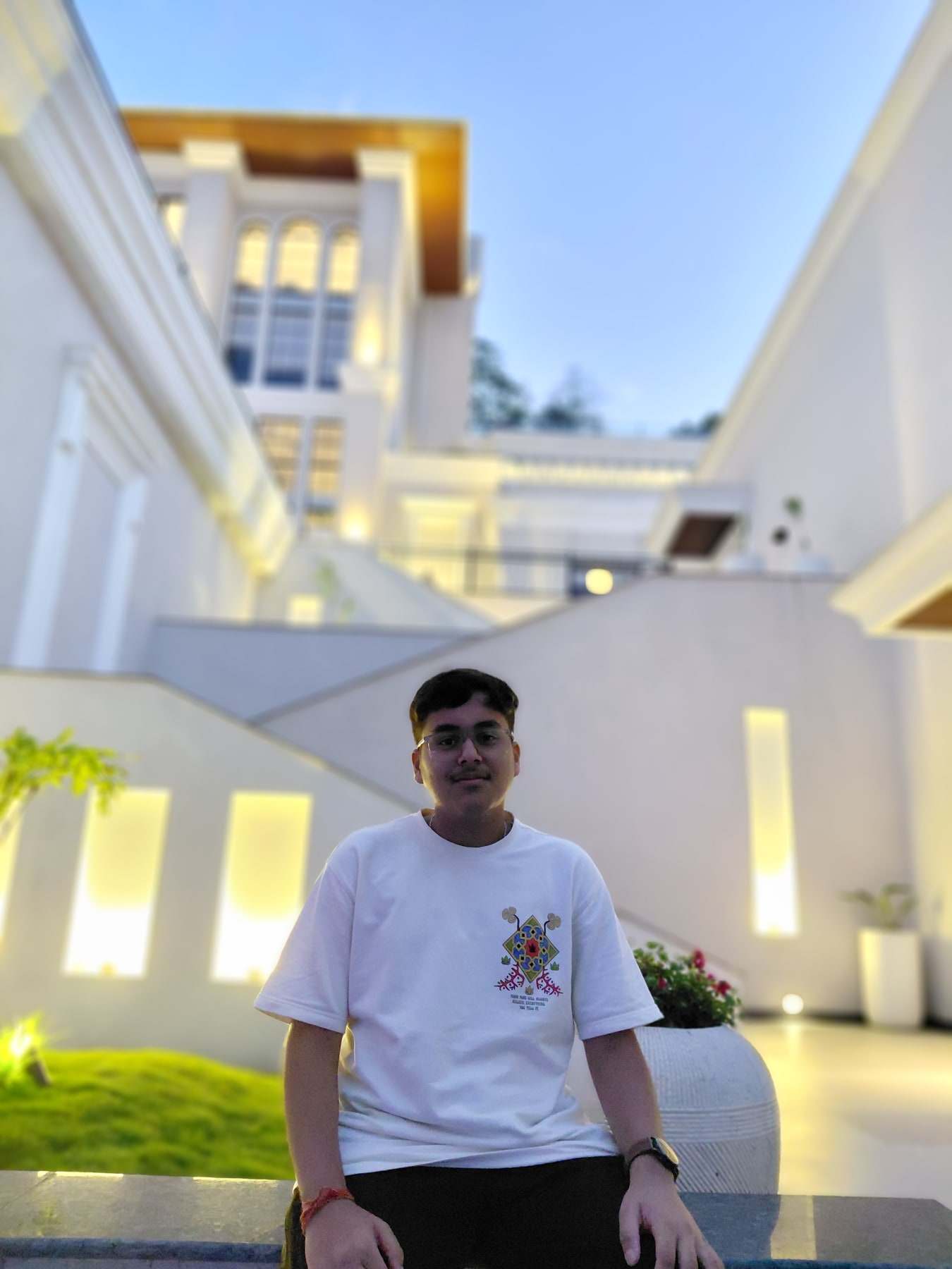 Harshit Murarka in a white T-shirt, seated outside a lit white building at dusk